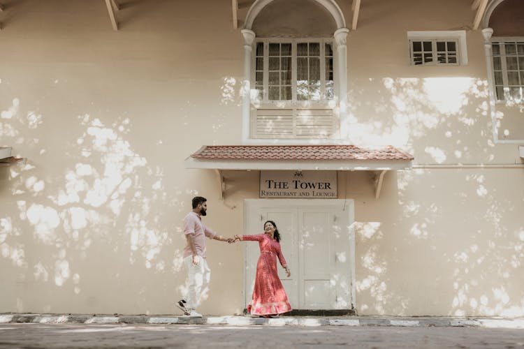 Woman Leading Man By Hand Towards Restaurant Entrance