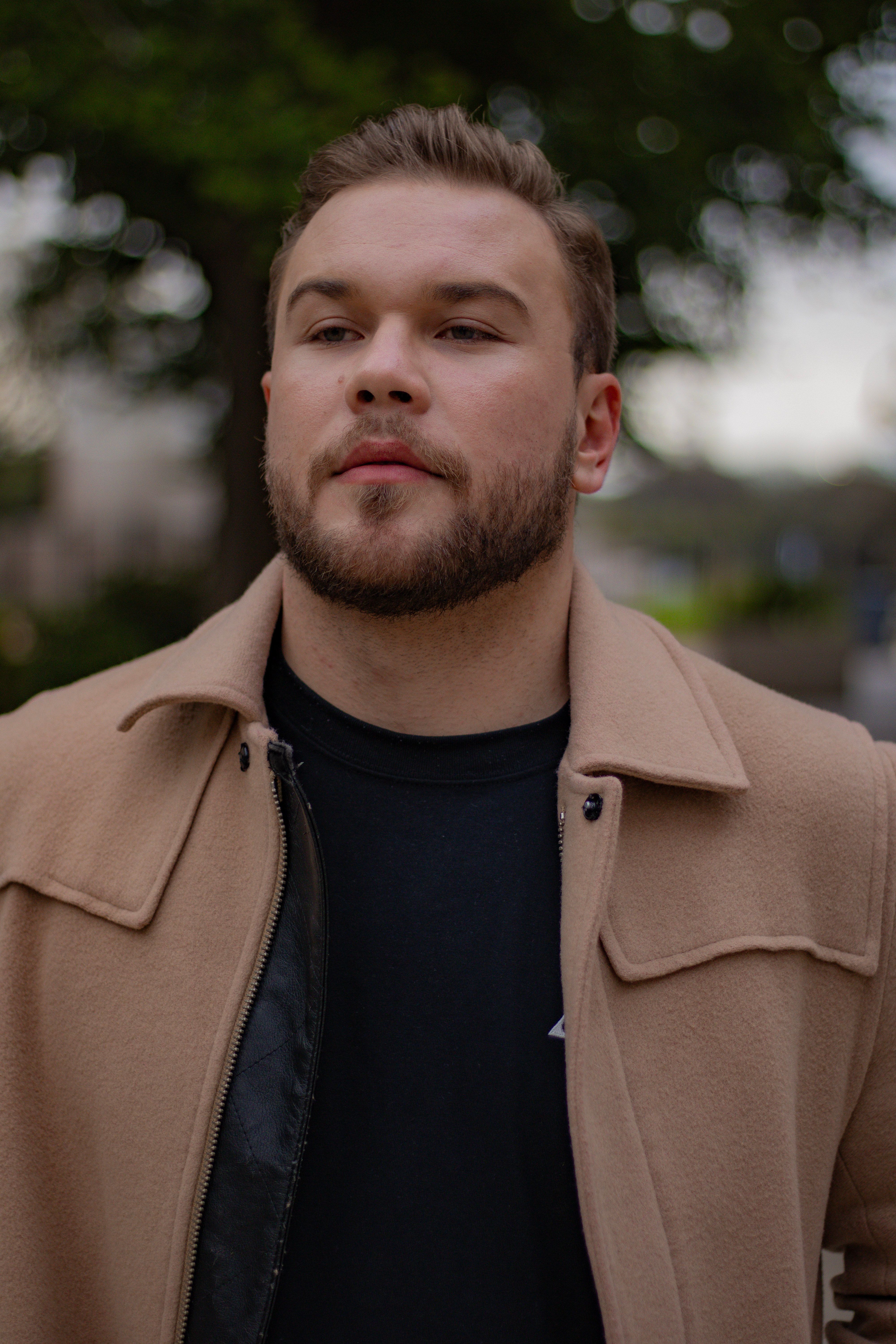 Bearded man in a fashionable beige coat enjoying a crisp fall day outdoors.