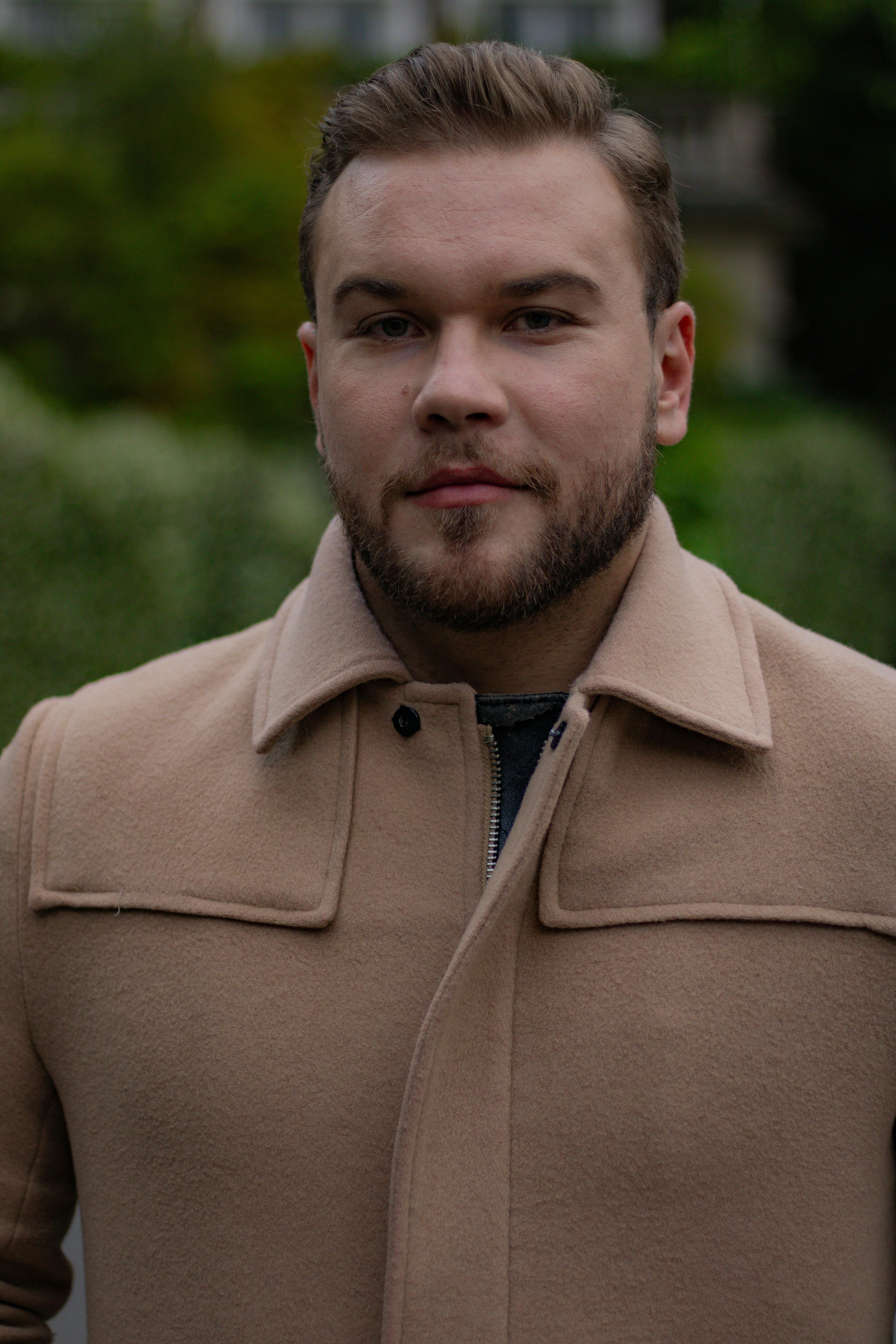 Stylish portrait of a man with a beard wearing a beige coat outdoors. Fashion photography.