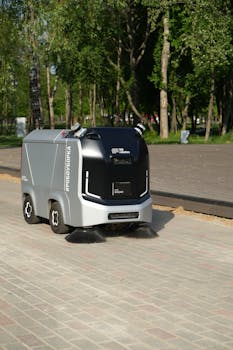 A robotic street sweeper operates autonomously on a city pavement under sunny conditions.