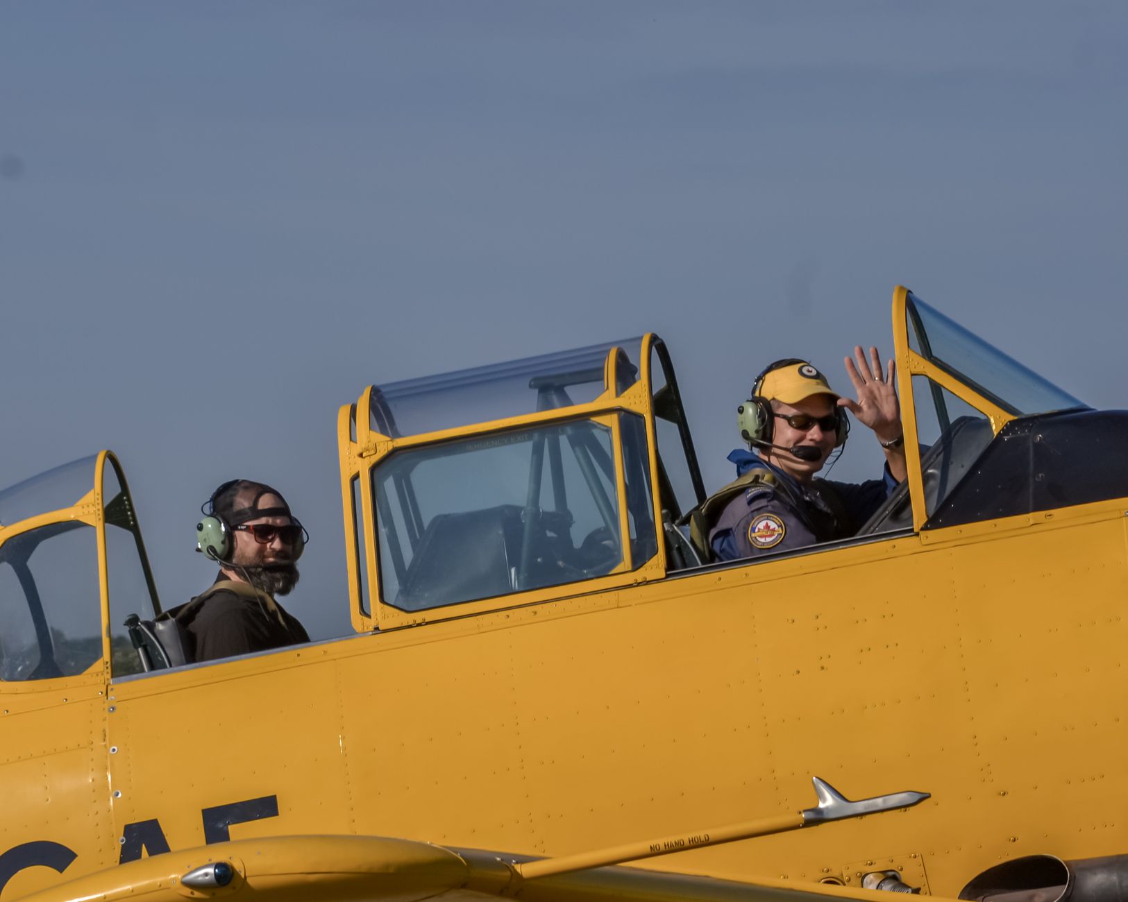 Two pilots in vintage aircraft cockpit, one waving, showcasing historic aviation charm.