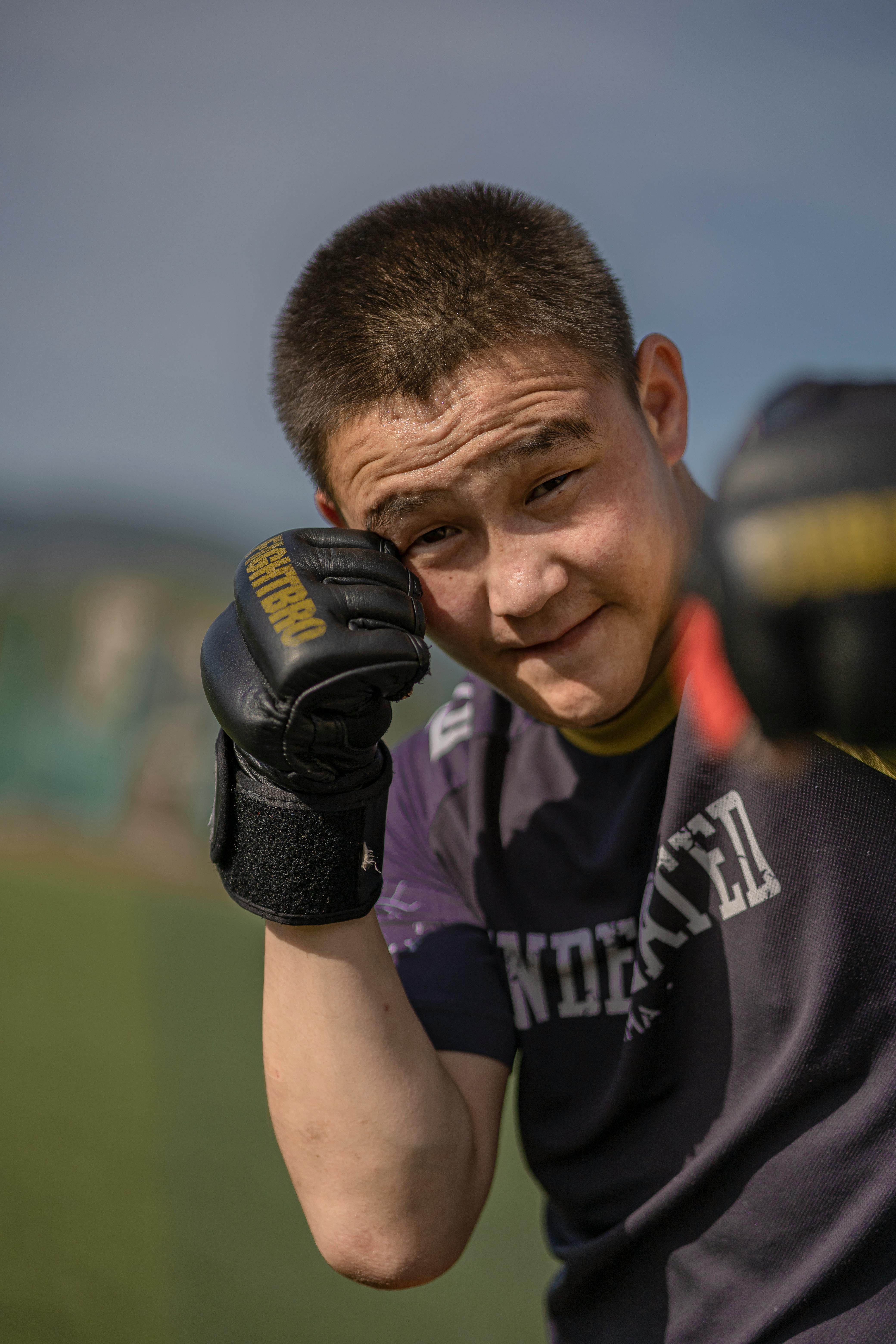 Portrait of a young Asian man in boxing gloves, training outdoors during the day.