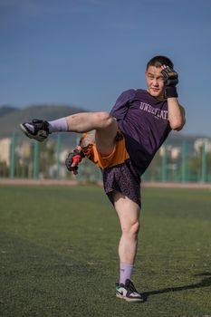A young male athlete warming up on a sunny day in a stadium, wearing sports attire.