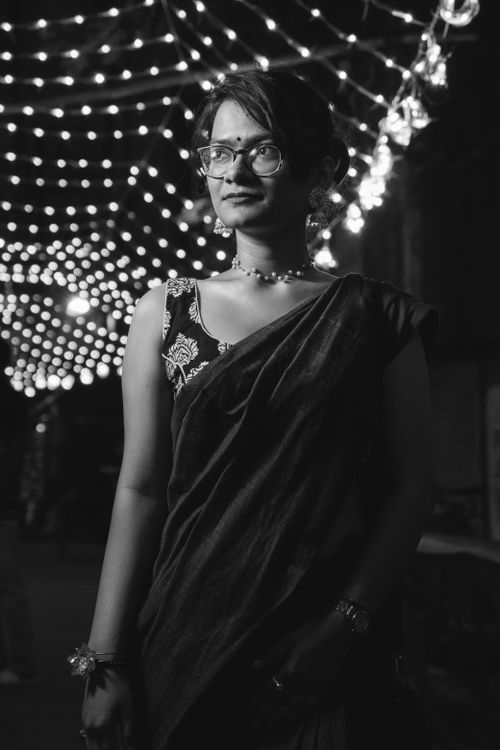 Free A young woman in a saree stands gracefully under illuminated festive lights, creating a moody atmosphere. Stock Photo