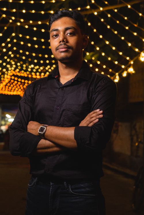 Free Man in black shirt posing confidently under string lights in a nighttime urban setting. Stock Photo