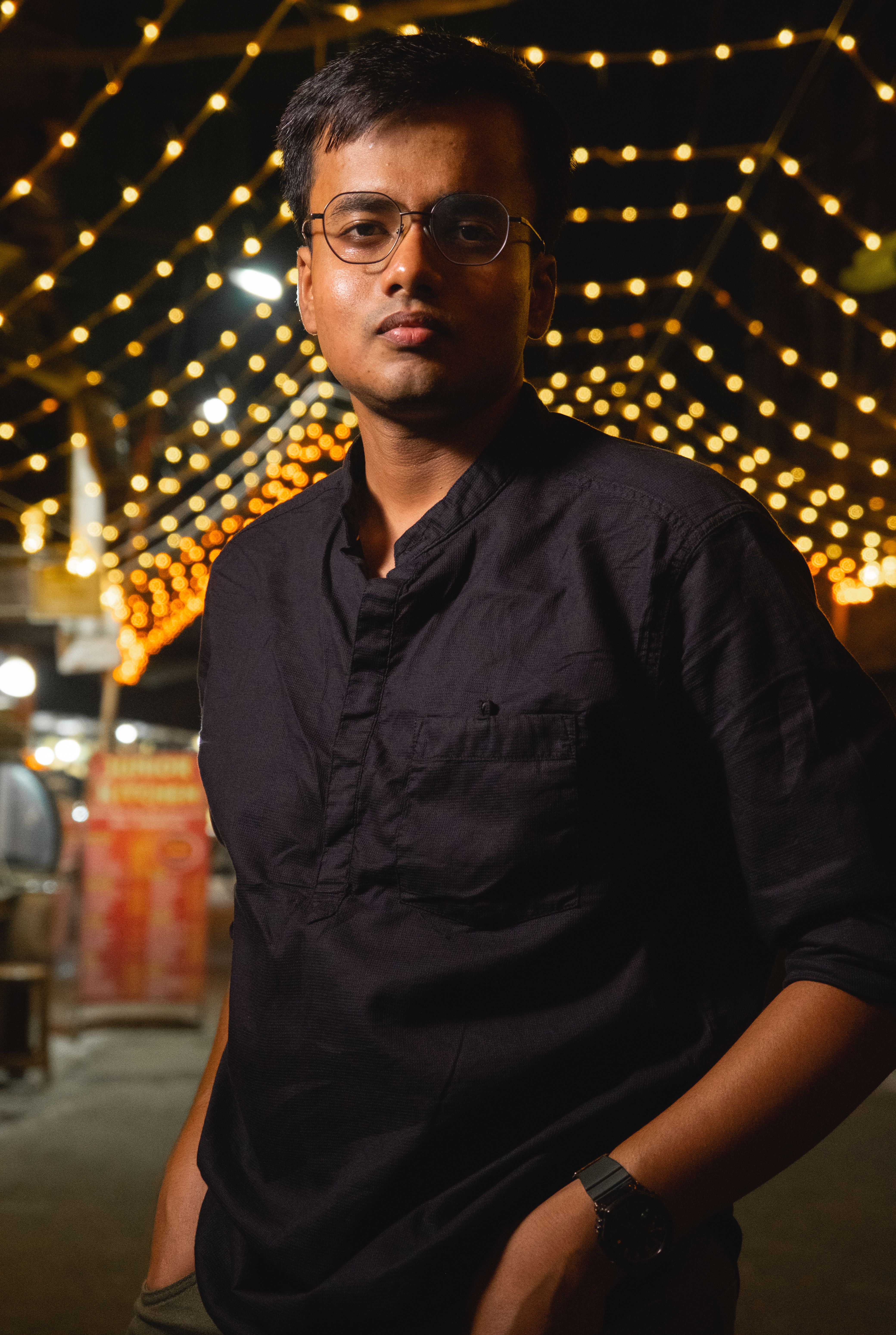 A young man standing under warm illuminated string lights at night.