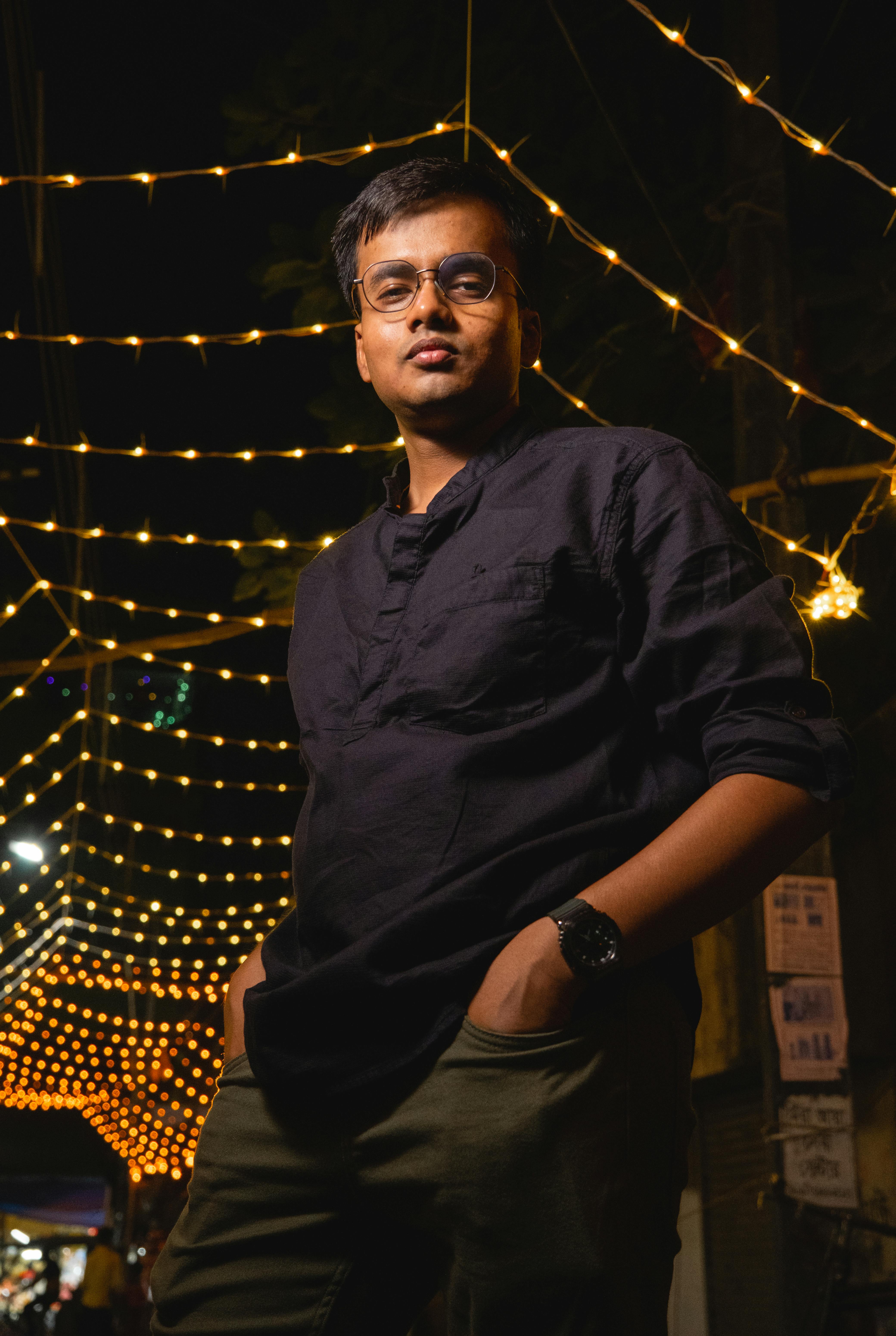 Man in black shirt posing confidently under street lights at night.