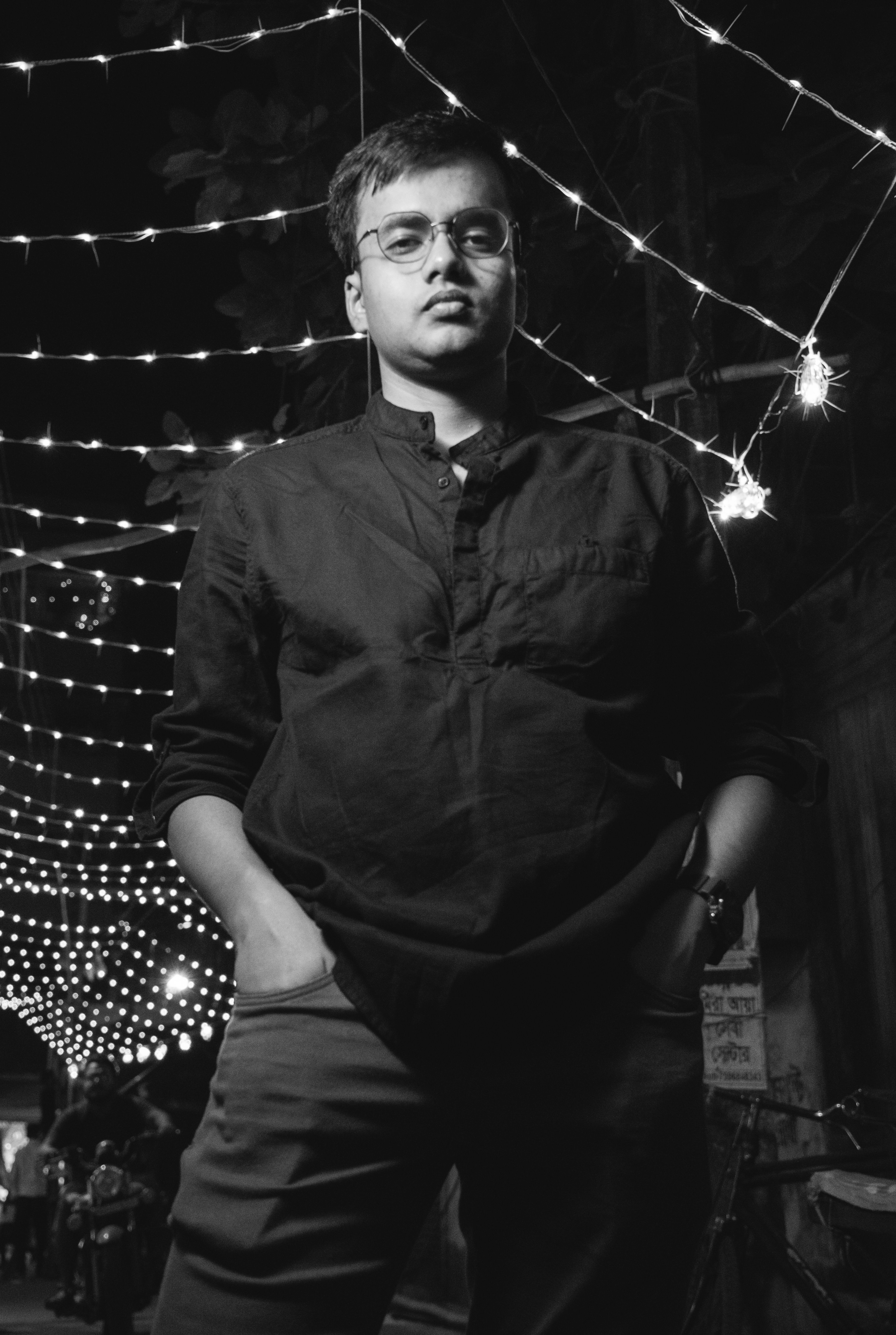 Black and white portrait of a man under string lights, showcasing confidence and style.