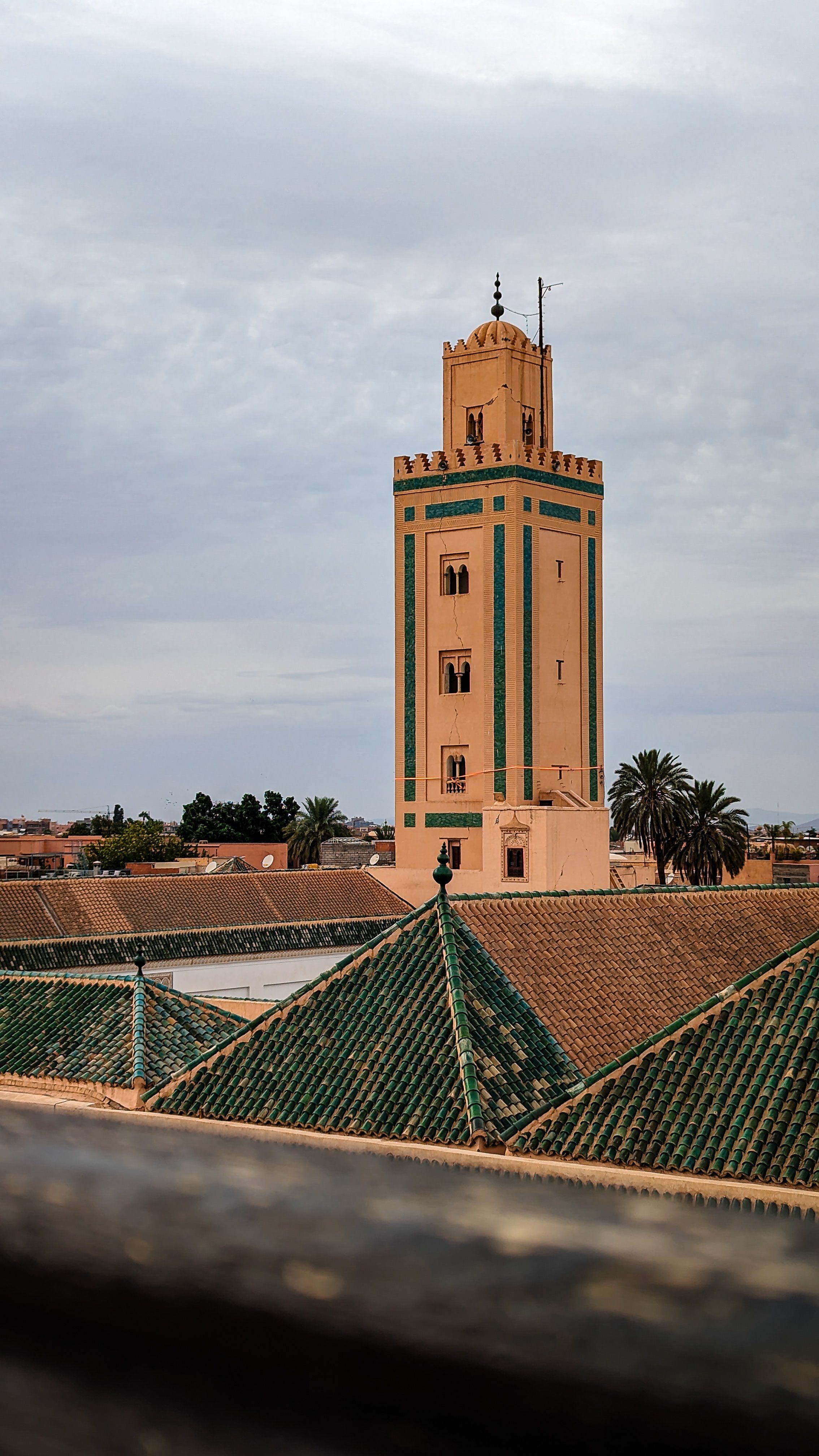 A vertical shot of the Ben Youssef Mosque tower against a cloudy sky in Marrakesh, Morocco.