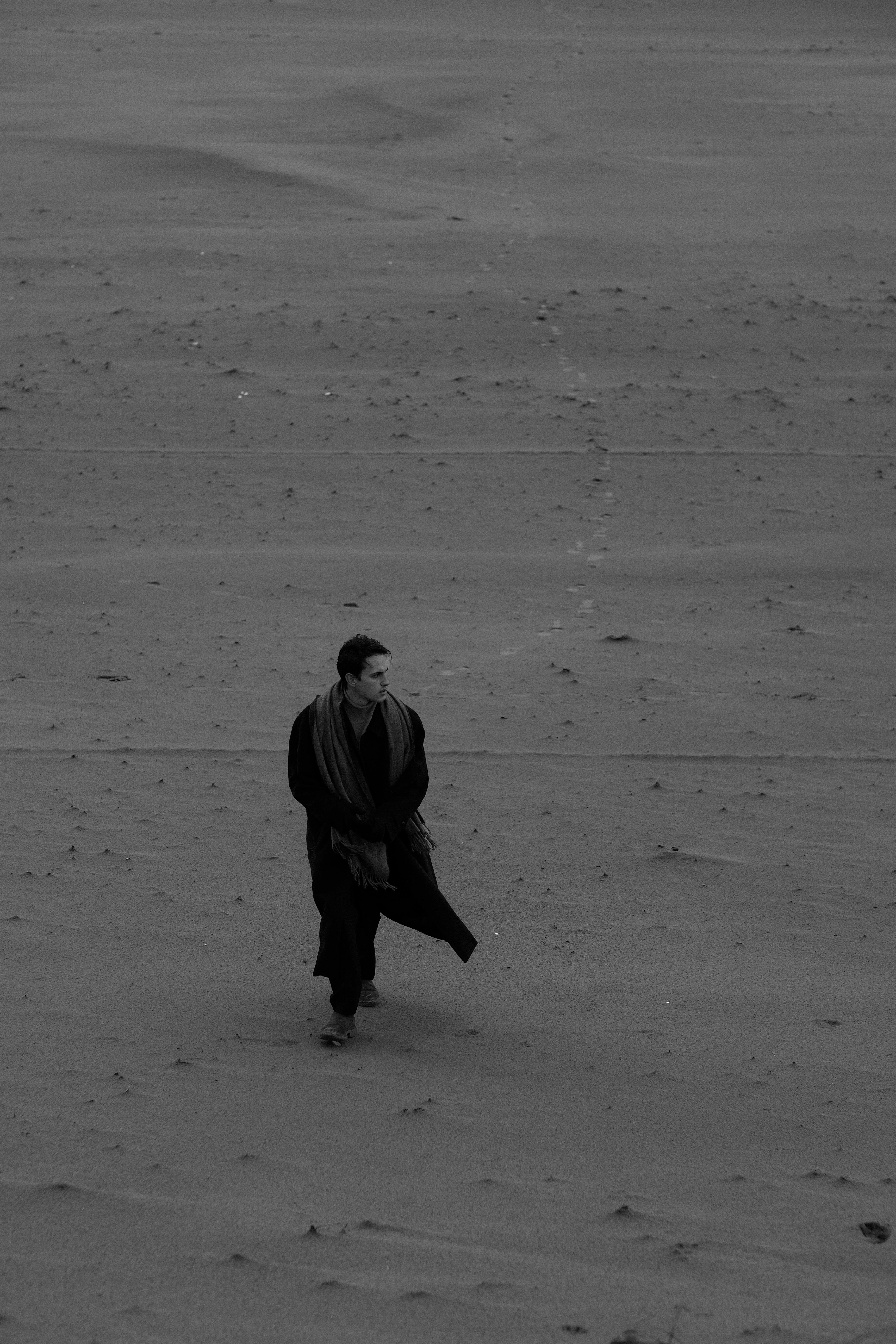Man with coat walking alone on a barren beach, black and white photo.