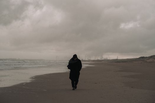 A person walks alone on a windy and overcast beach, creating a moody atmosphere.