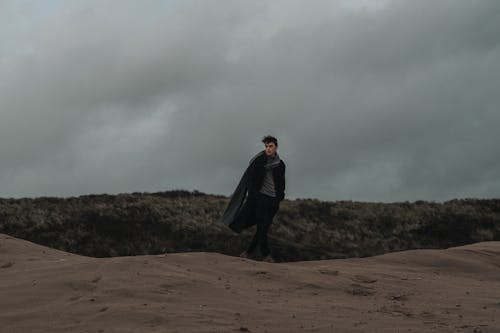 Free Man in Elegant Black Coat and Long Gray Scarf Walking on a Beach Dune Stock Photo