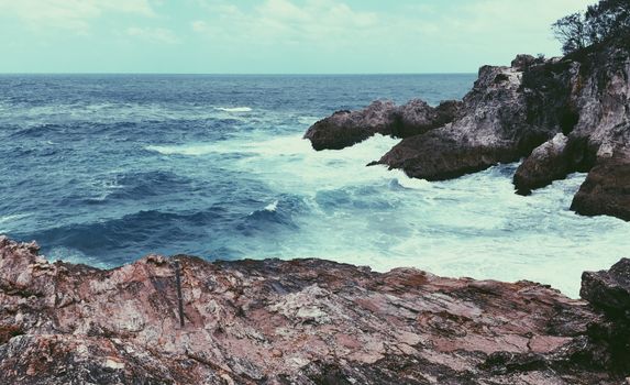 A stunning view of rugged coastal rocks with waves crashing and vast sea horizon.