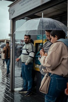 People using umbrellas at a bus stop during rain, showcasing public transit and urban life.