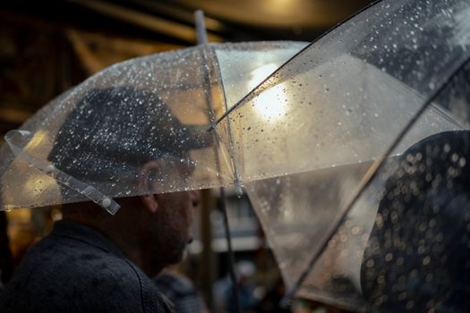 A man with a transparent umbrella walking through a rainy city street, capturing the essence of urban lifestyle in wet weather.