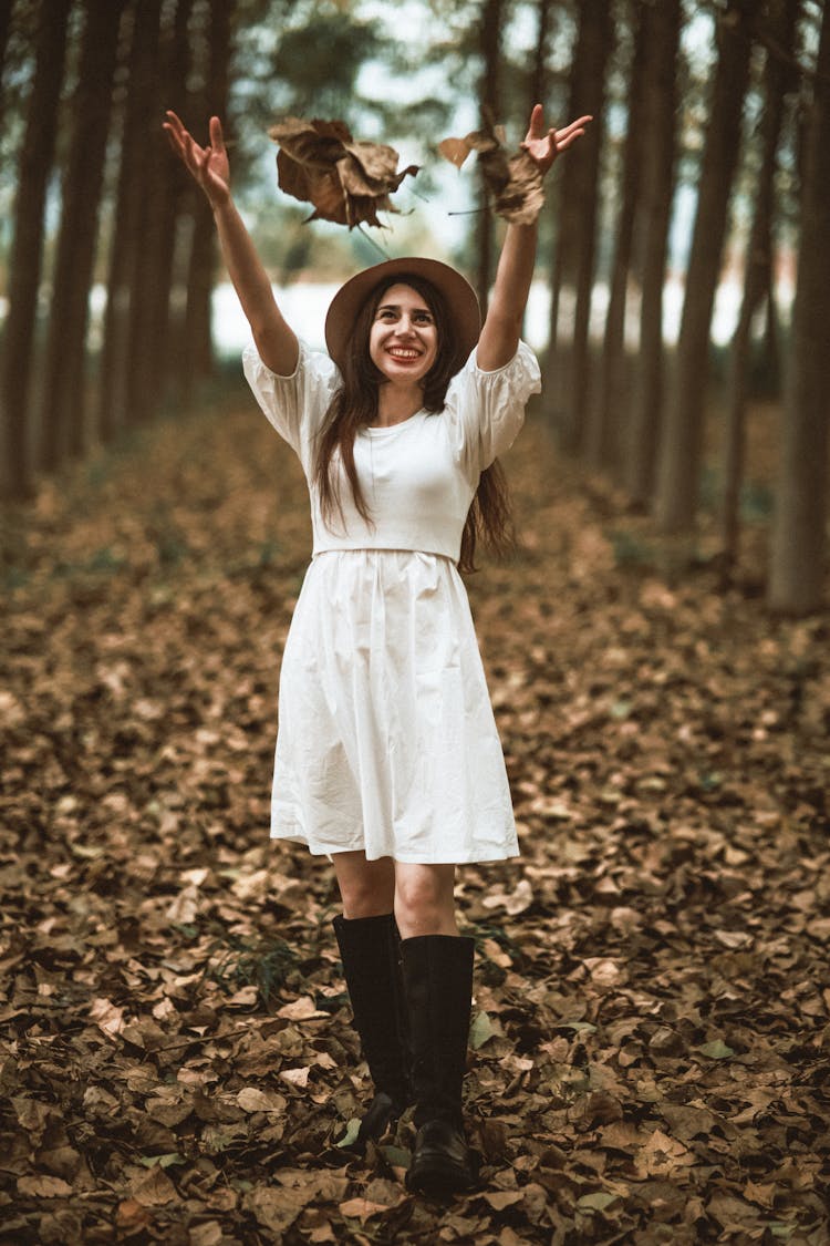 Young Woman Throwing Autumn Leaves In A Forest 