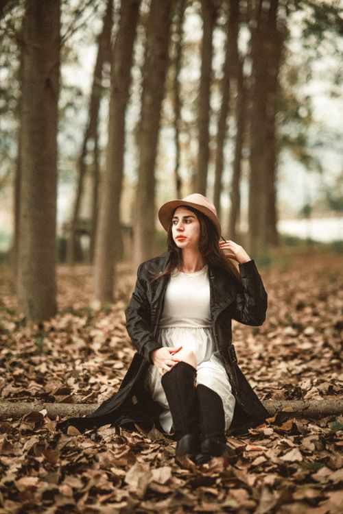 Free Caucasian woman in a black coat and hat sits gracefully in a park during fall. Stock Photo