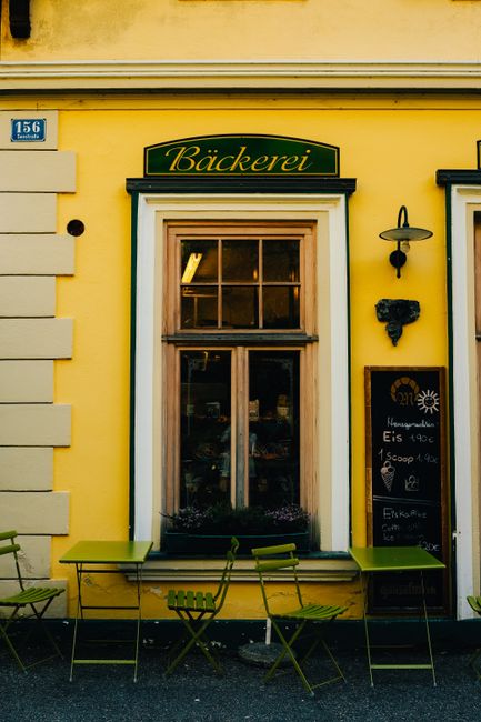 Charming bakery facade with yellow walls, green chairs, and window display.