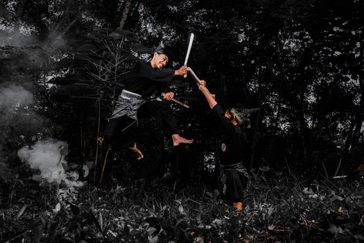 Two martial artists engaged in a high-flying sword fight in a dense forest.