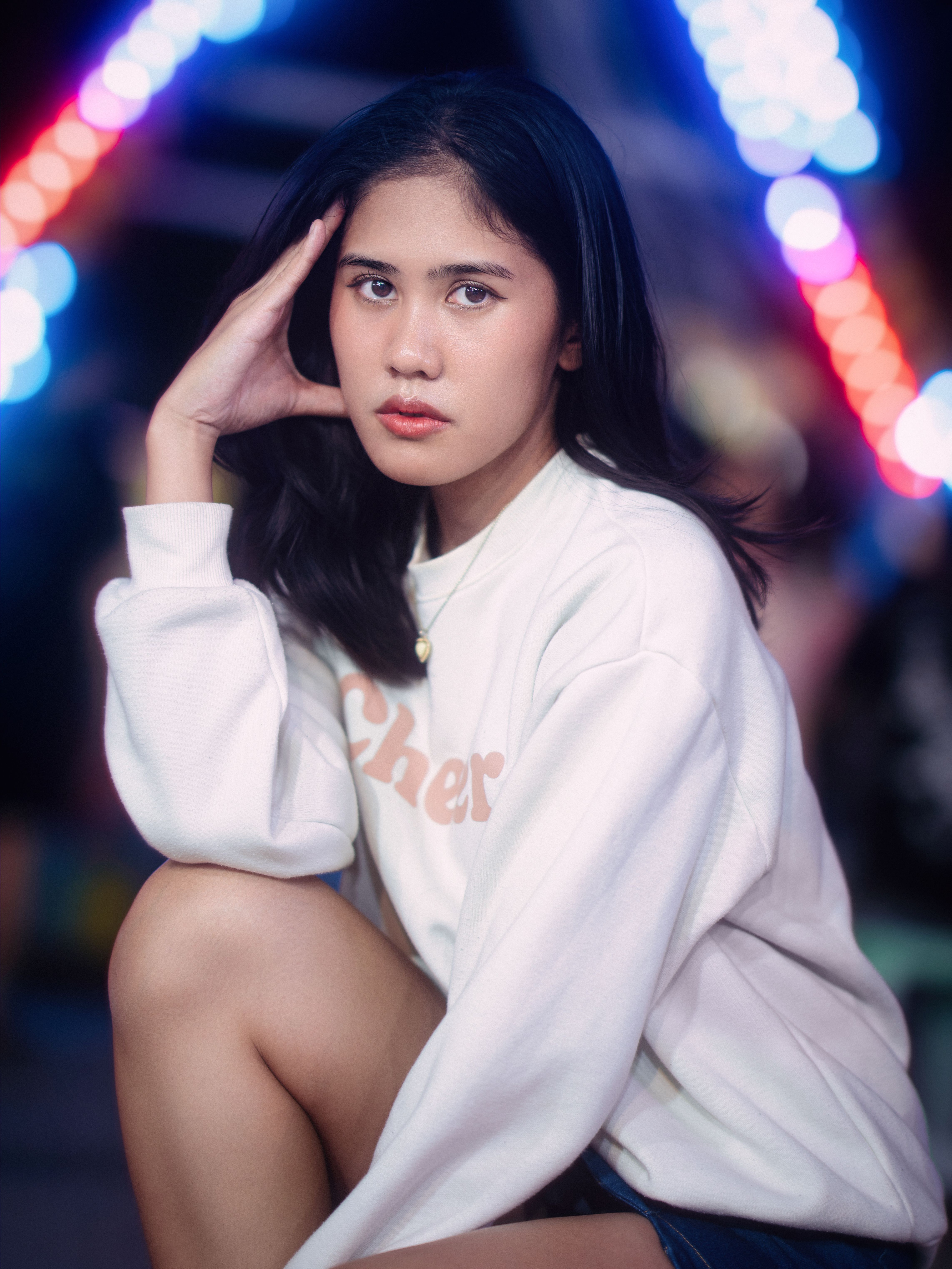 Elegant portrait of a woman wearing a white sweatshirt, captured with colorful bokeh lights in the background.