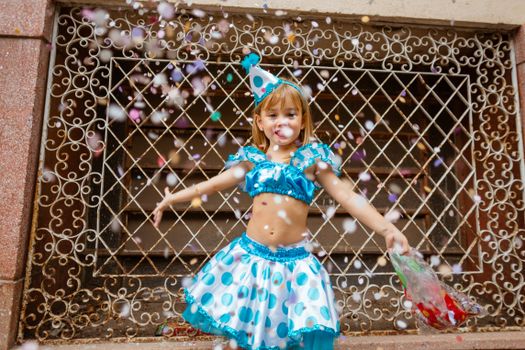 A child in a festive outfit enjoys a party with confetti and a vibrant atmosphere outdoors.