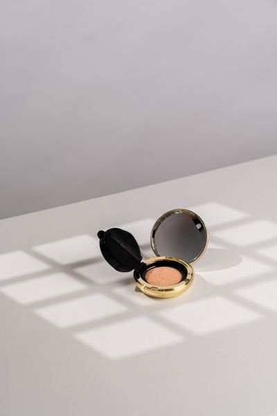 Gold refillable compact open on a sunlit surface. Photo by Moni Rathnak on Pexels