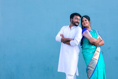 Free A happy couple in traditional Indian clothing standing against a blue backdrop, smiling at each other. Stock Photo