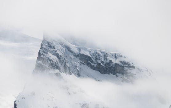 Ethereal view of a snow-covered mountain peak shrouded in mist, creating a serene and mysterious atmosphere.