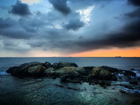 Stunning sunset over rocky shores with cargo ships on the horizon in Galle, Sri Lanka.