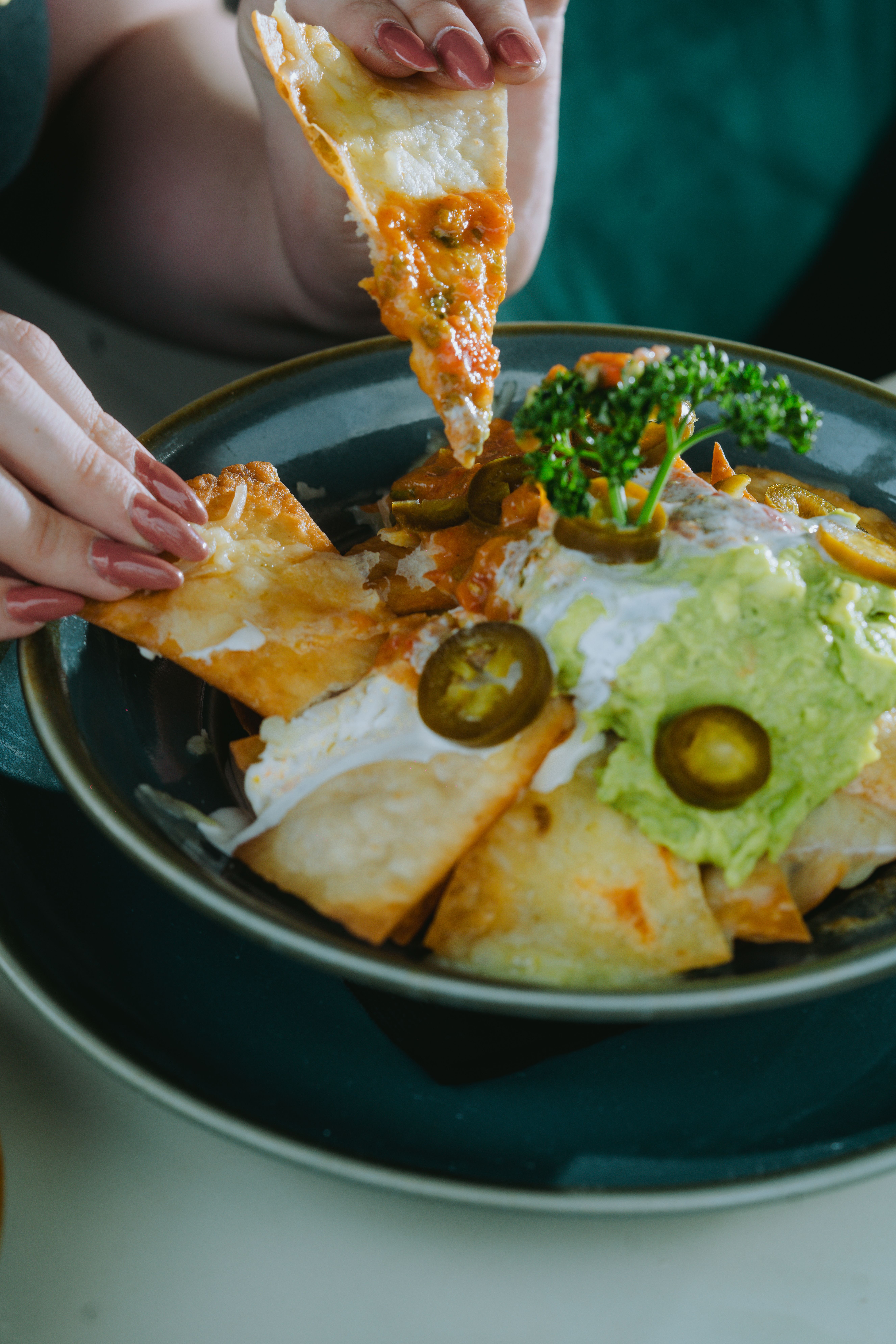 Tantalizing plate of nachos topped with cheese, guacamole, and jalapenos being enjoyed as a snack.
