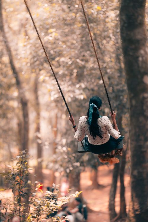 Free A woman enjoys a peaceful swing ride in a sunlit forest, evoking relaxation and tranquility. Stock Photo