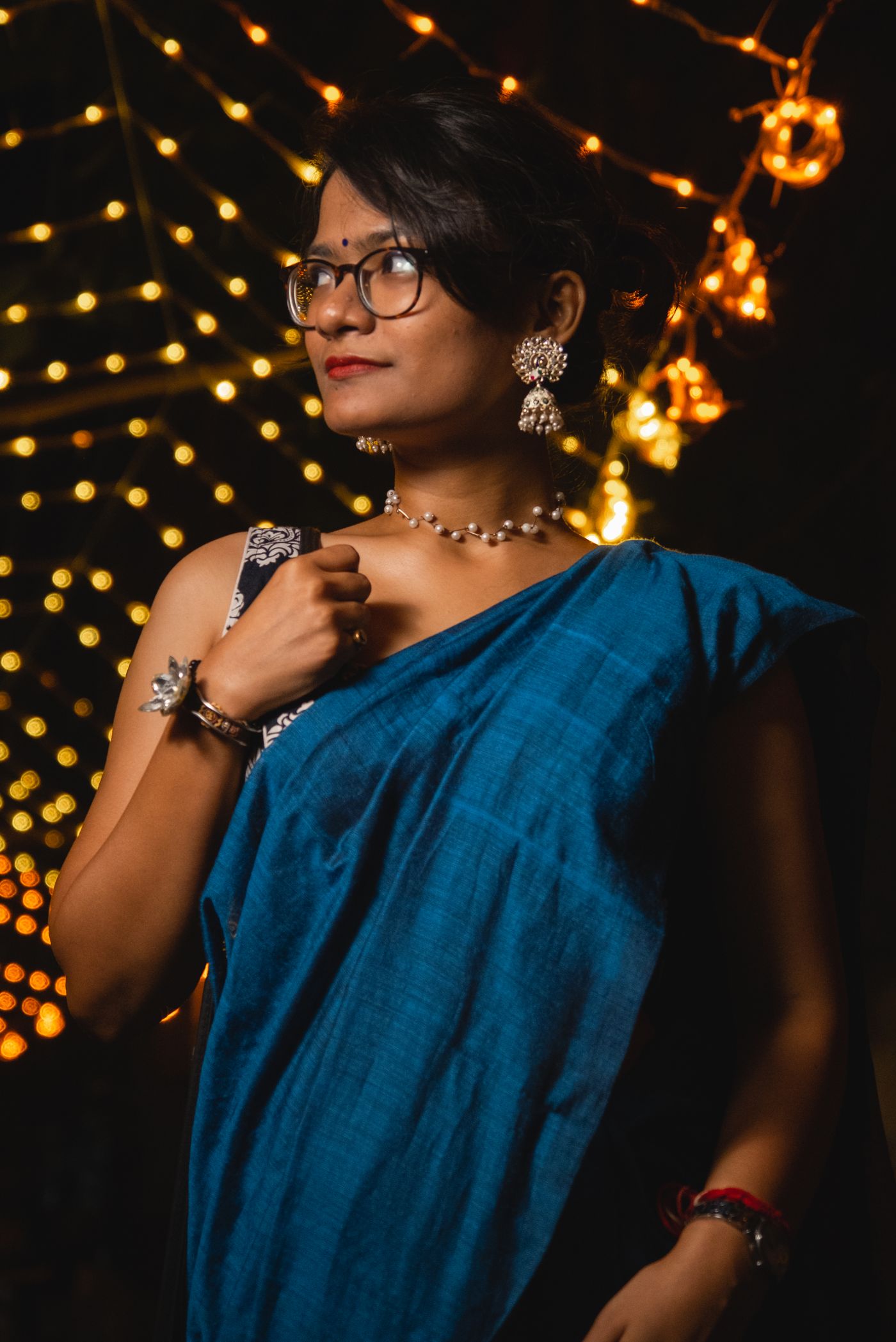 Stylish Indian woman in blue saree wearing party jewellery against festive evening lights