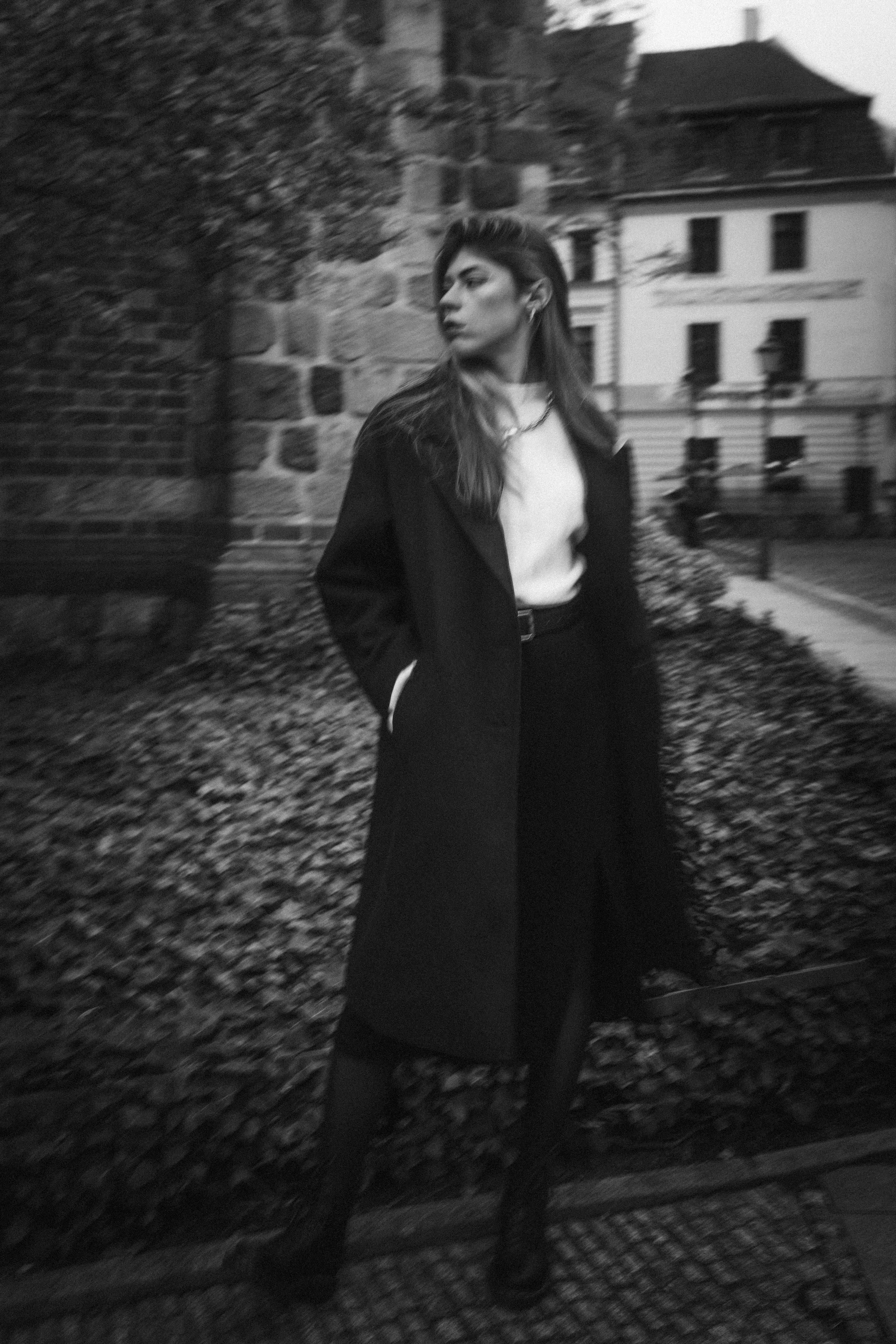 Black and white portrait of a woman posing in a stylish coat outdoors on a city street.