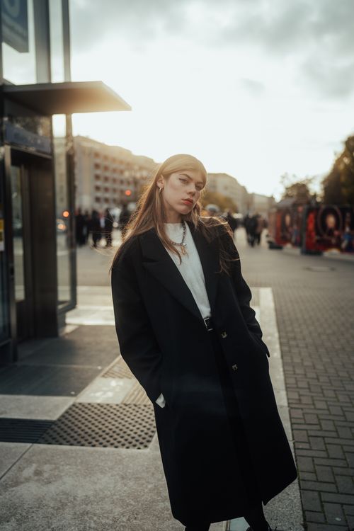 Free Stylish woman in a dark coat poses confidently on a sunny city street in fall. Stock Photo