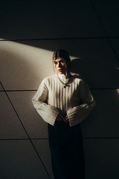 Fashion-forward woman in a stylish sweater and skirt, captured in dramatic sunlight with artistic shadows.
