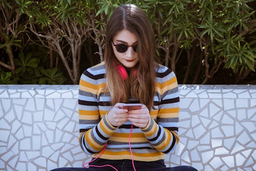 Fashionable young woman in sunglasses and headphones using a smartphone on a sunny day.