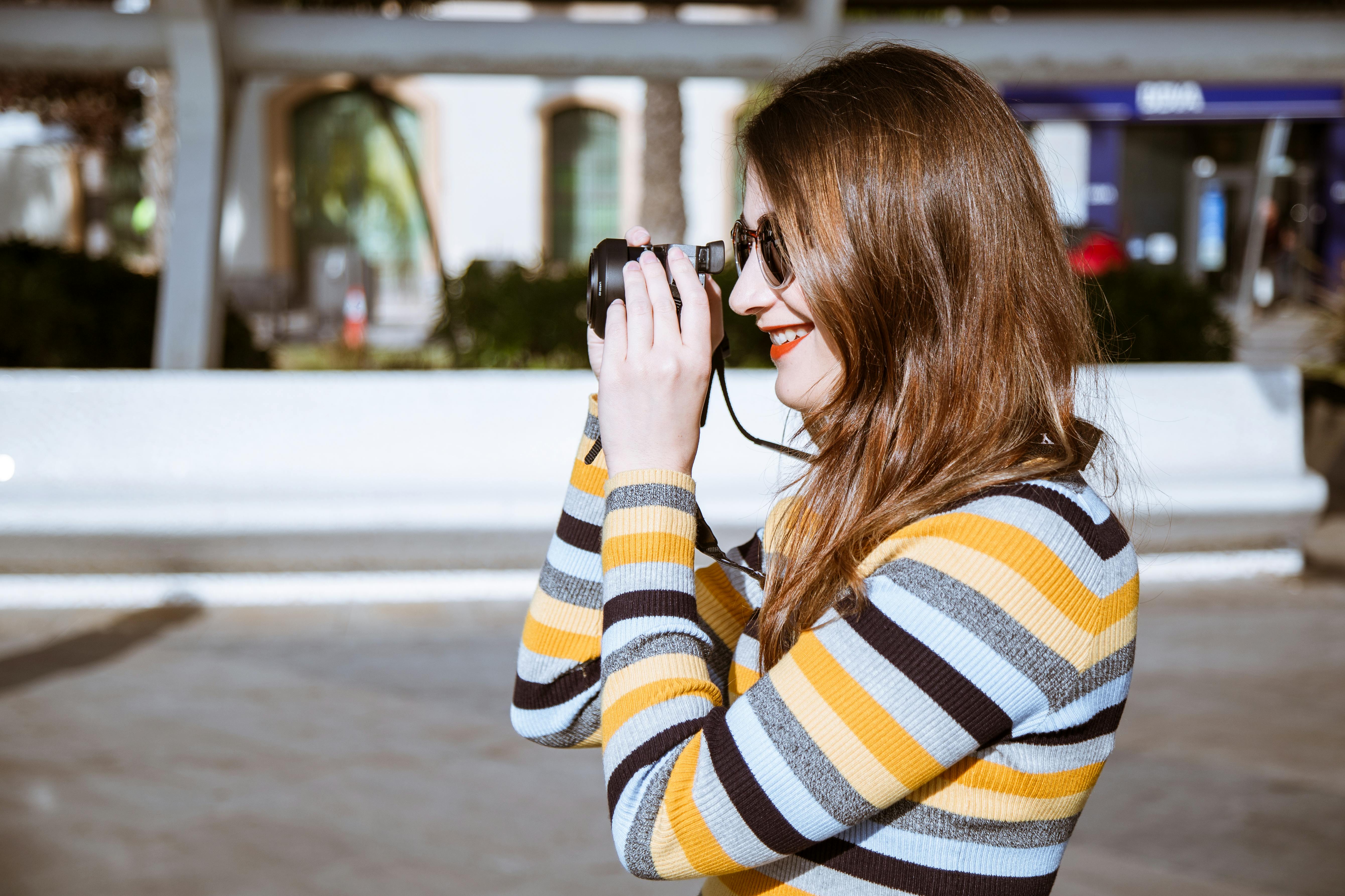 一个女人穿着条纹衣服，在户外用一个小相机拍照