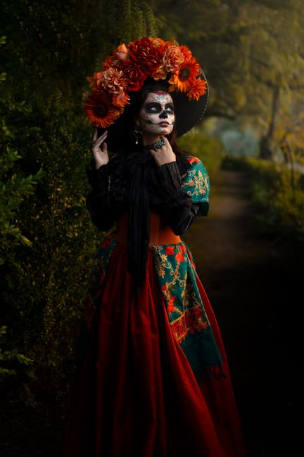 Woman in traditional Day of the Dead costume with floral garland in a dark, autumn setting.