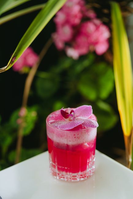 A refreshing pink cocktail garnished with a purple orchid, perfect for a tropical vibe.