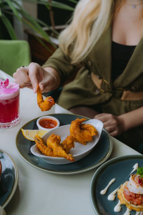 Free A woman dining indoors, enjoying crispy fried shrimp with a colorful cocktail. Stock Photo