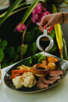 A gourmet roast beef dinner being elegantly poured with rich gravy, showcasing vibrant vegetables and classic accompaniments.