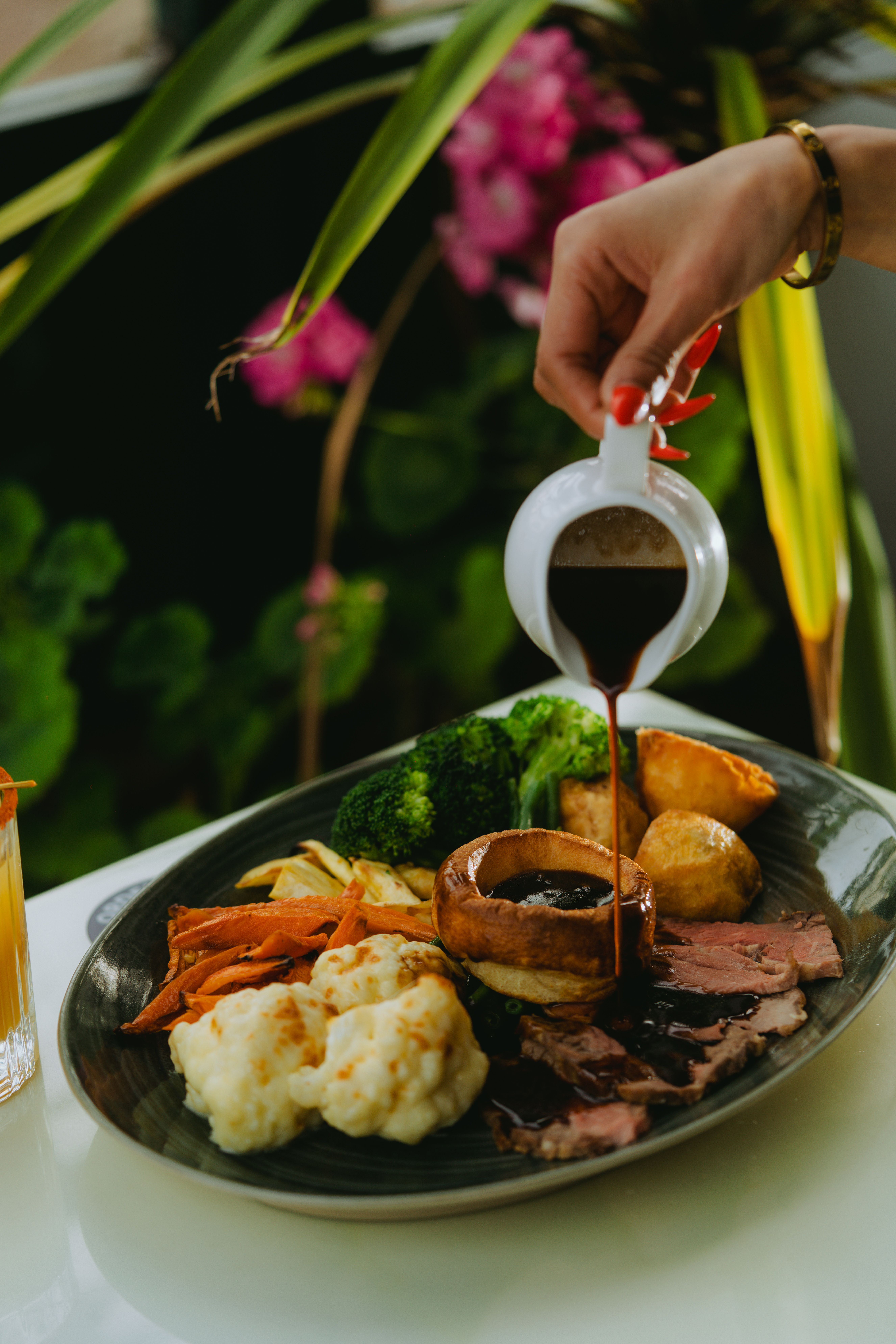 Close-up of a gourmet roast beef dinner with vegetables and gravy being poured.