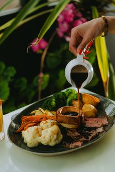 Close-up of a gourmet roast beef dinner with vegetables and gravy being poured.