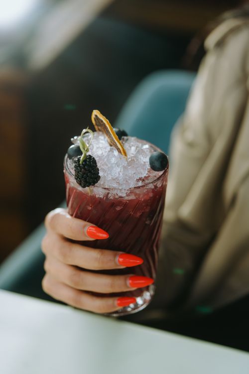 Free Close-up of a hand holding a berry-infused cocktail with ice in a glass, stylish setting. Stock Photo