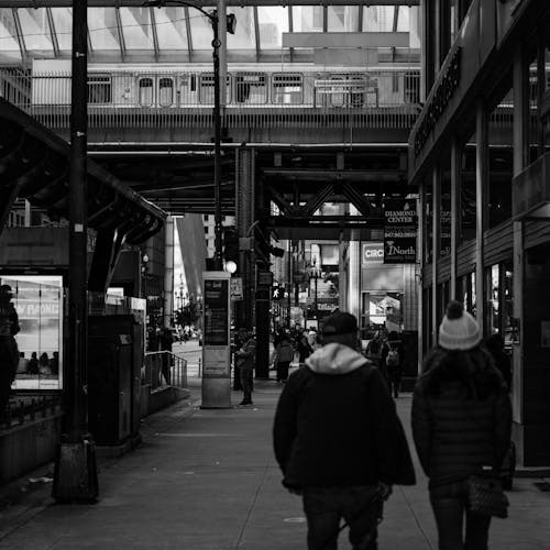 Woman and Man in Jackets Walking on Sidewalk in Black and White