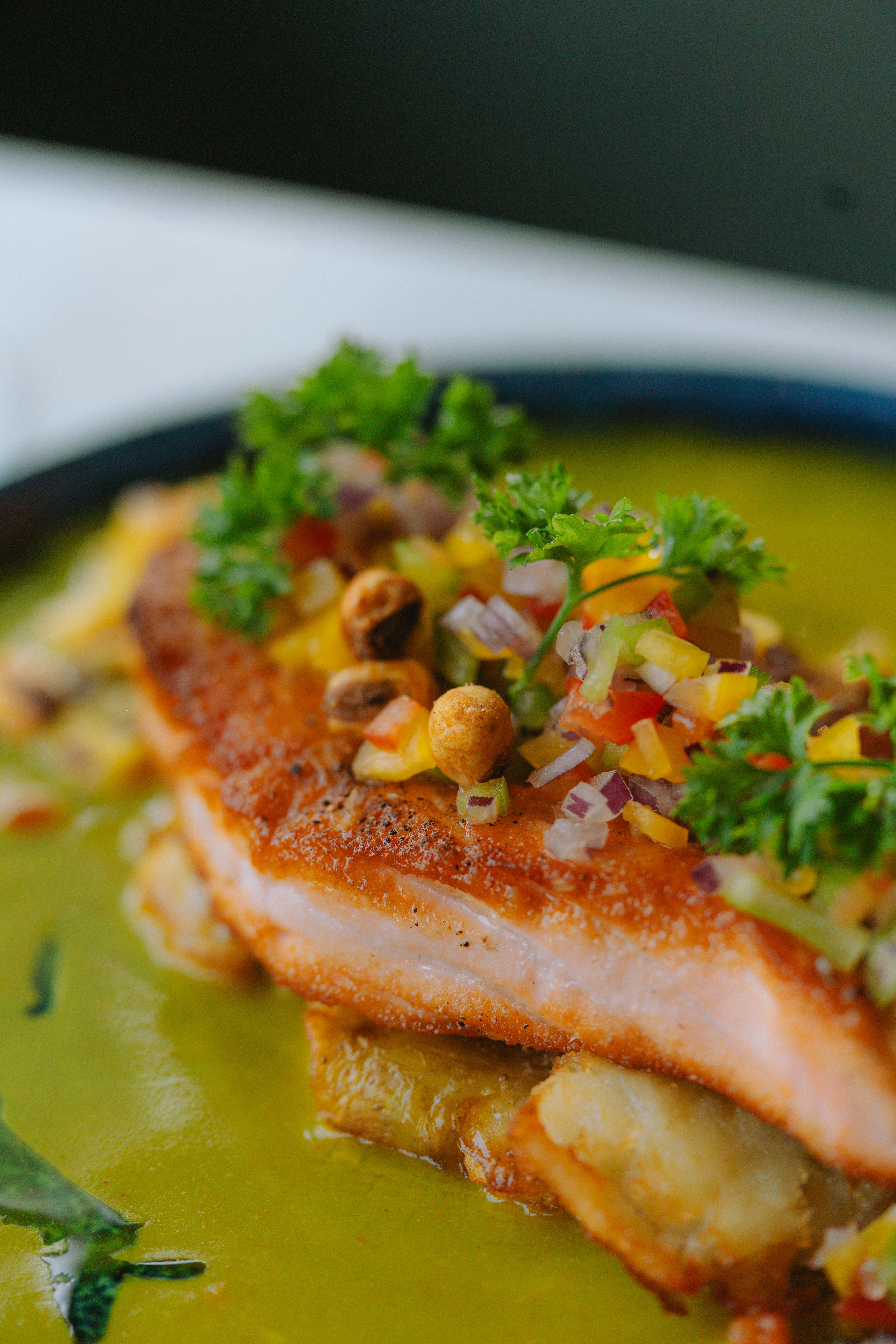 Golden-crusted Cajun salmon fillet topped with creamy green poblano butter sauce and fresh chives on a white dinner plate