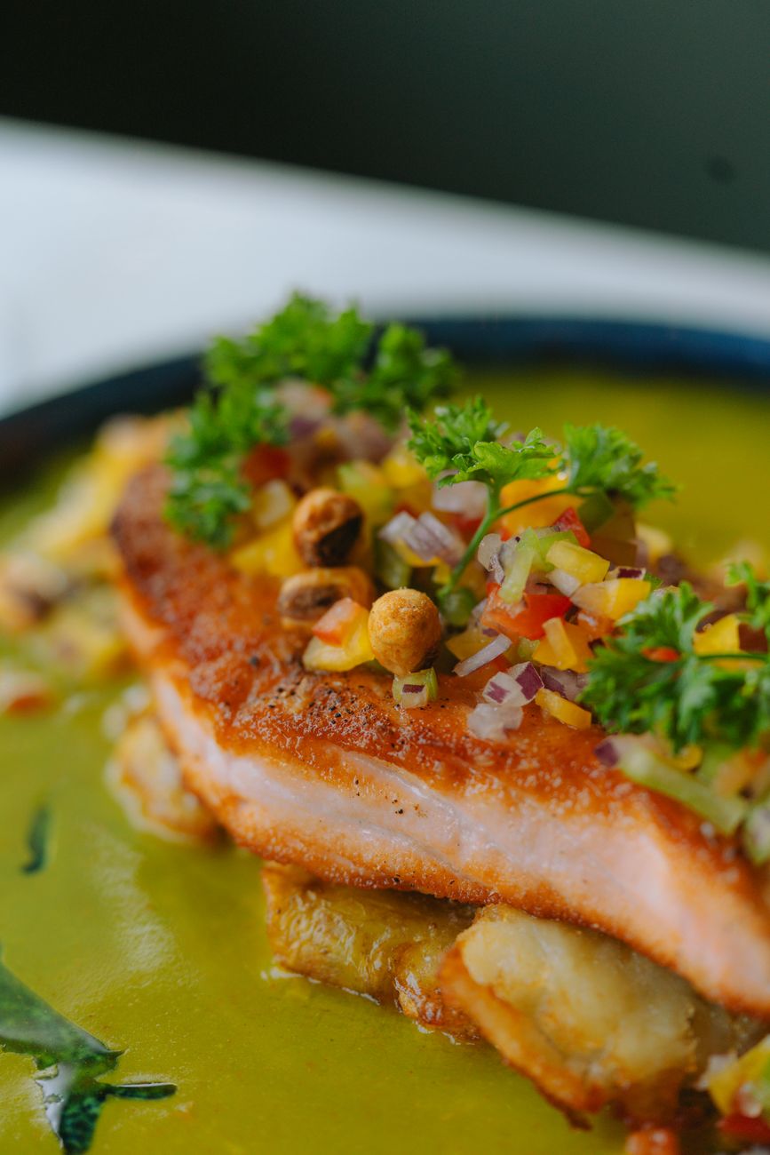 Golden-crusted Cajun salmon fillet topped with creamy green poblano butter sauce and fresh chives on a white dinner plate