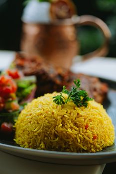 A close-up of a vibrant yellow rice dish served with fresh salad and grilled meat in an elegant dining setting.