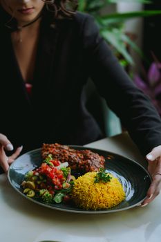 A woman enjoying a colorful and artistic dish indoors, featuring rice and vegetables.