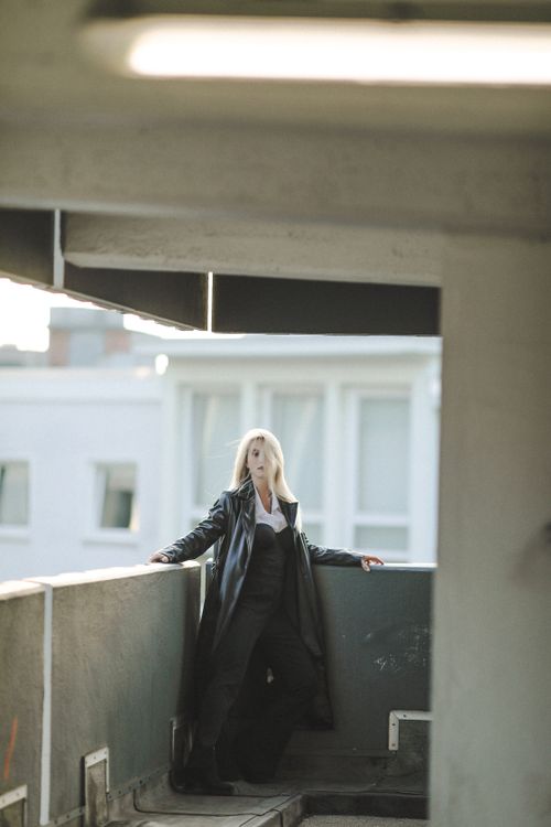 Free Blonde woman in a black coat poses elegantly in an urban environment. Stock Photo